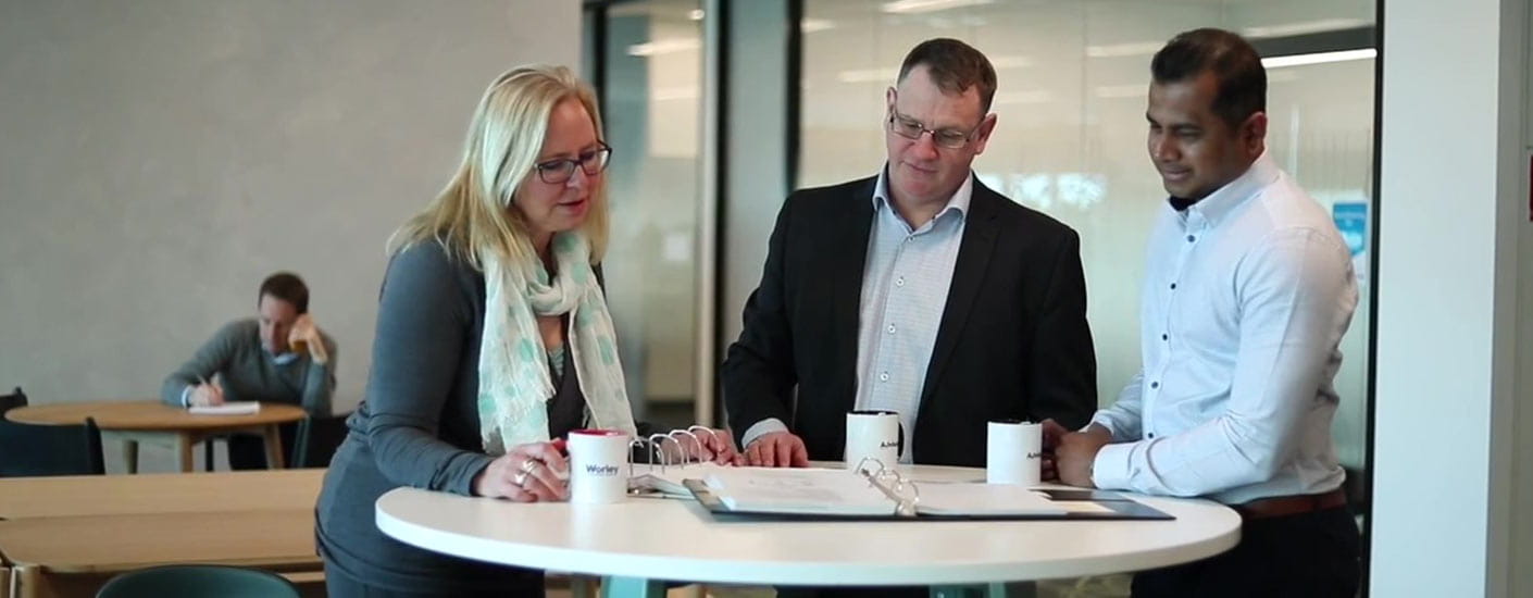 Three people of Advisian, talking together at a desk in the office.