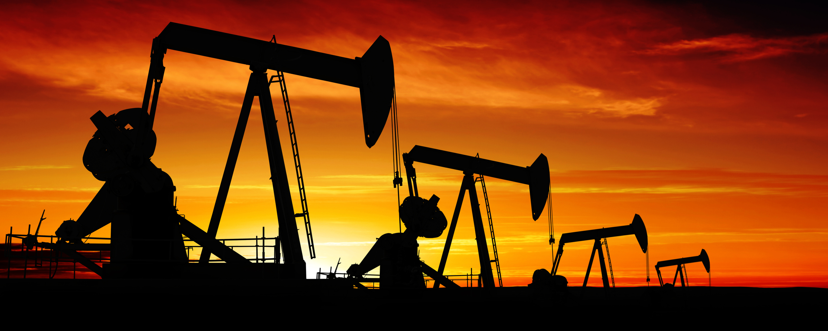 Four oil pumps in a row, with an orange sky and setting sun in the background. 