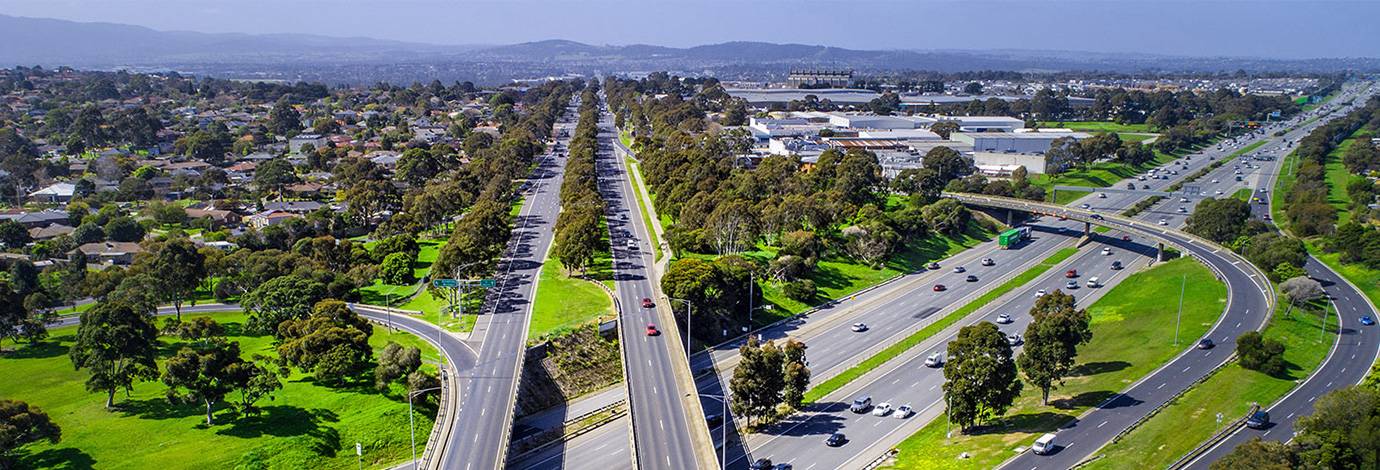 Aerial view of a highway in a suburban area with trees and mountains in the distance.