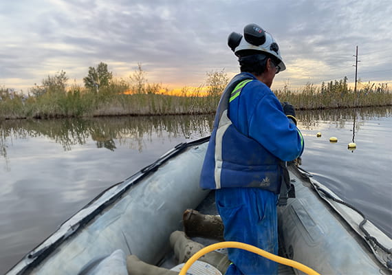 A person wearing protective clothing in a boat on a body of water.