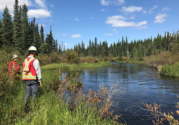 Two people in PPE standing at the edge of a river in Cold Lake, Alberta